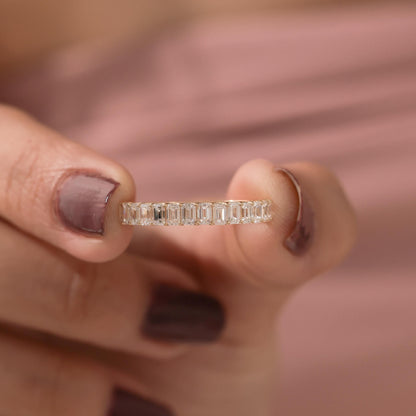 Close-up of hand holding Emerald Cut Eternity Wedding Ring, highlighting moissanite sparkle and yellow gold band.