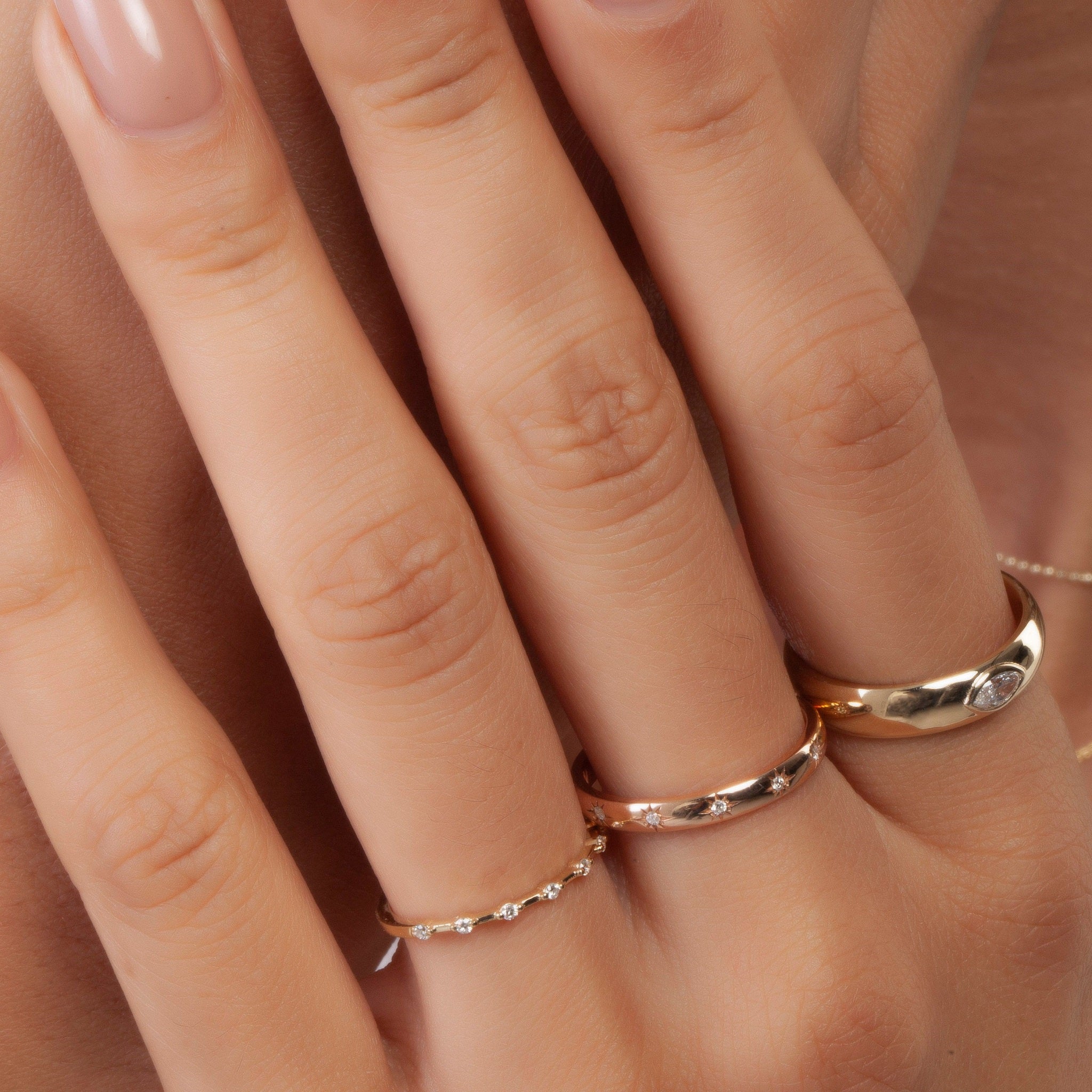 Model wearing minimalist yellow gold diamond wedding band with pavé-set lab diamonds, styled with other rings for a layered bridal look.