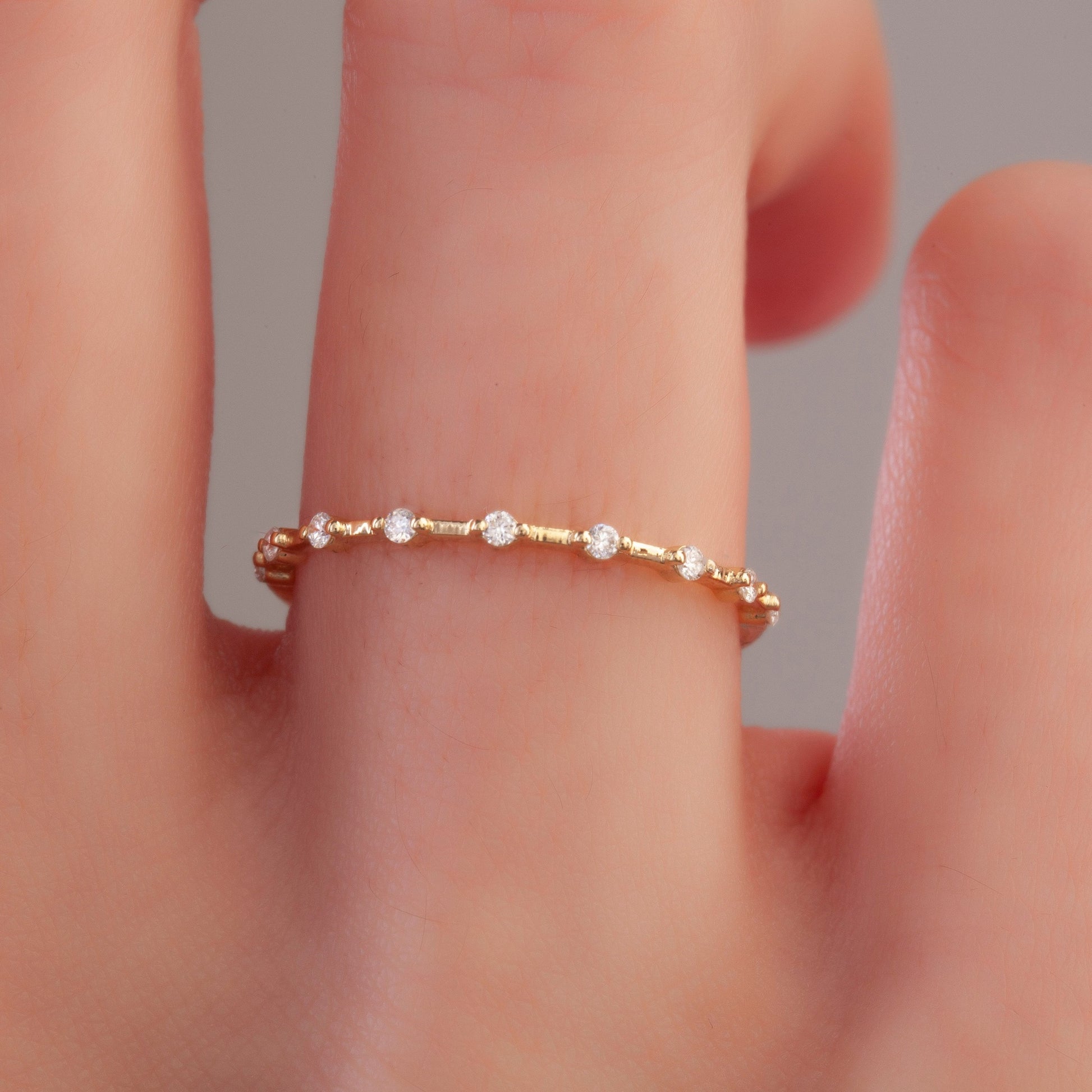 Close-up of minimalist yellow gold diamond wedding band on finger, showcasing round pavé-set lab diamonds and slender band design.