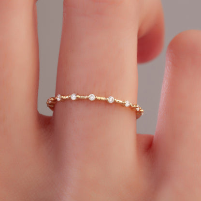 Close-up of minimalist yellow gold diamond wedding band on finger, showcasing round pavé-set lab diamonds and slender band design.