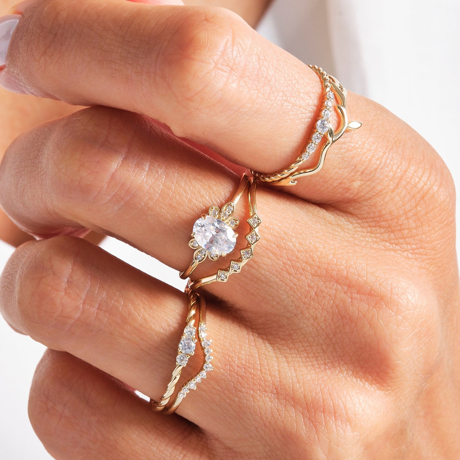 Stacked gold rings on hand featuring the Seven Stone Twisted Rope Braided Diamond Wedding Ring paired with matching diamond bands.