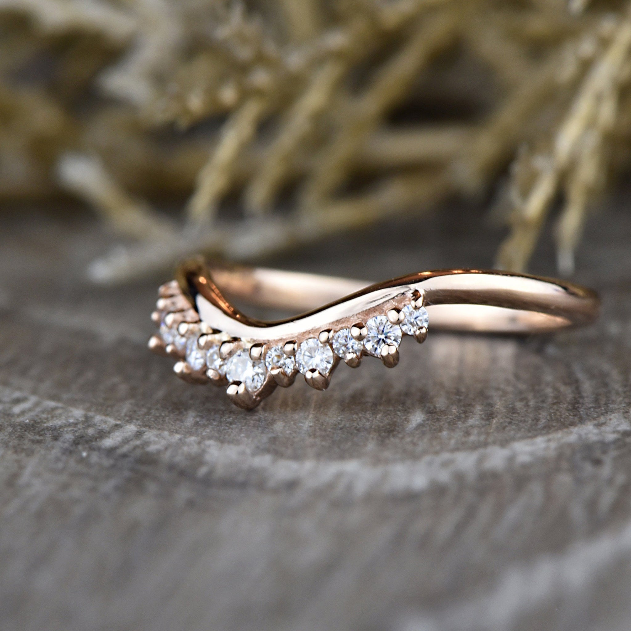 Close-up of rose gold Round Diamond Tiara Ring on wood surface, featuring chevron band and prong-set diamonds.