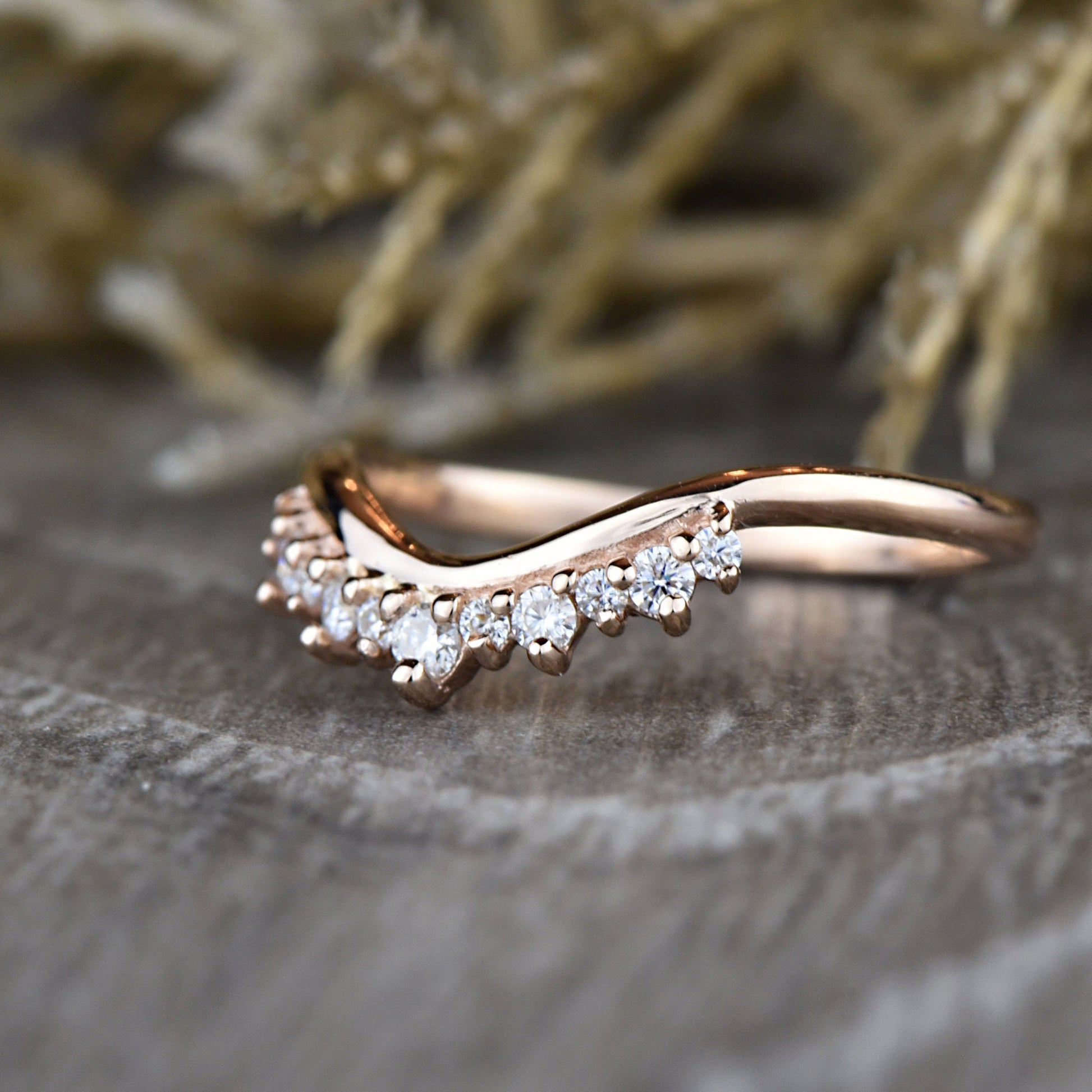 Close-up of rose gold Round Diamond Tiara Ring on wood surface, featuring chevron band and prong-set diamonds.
